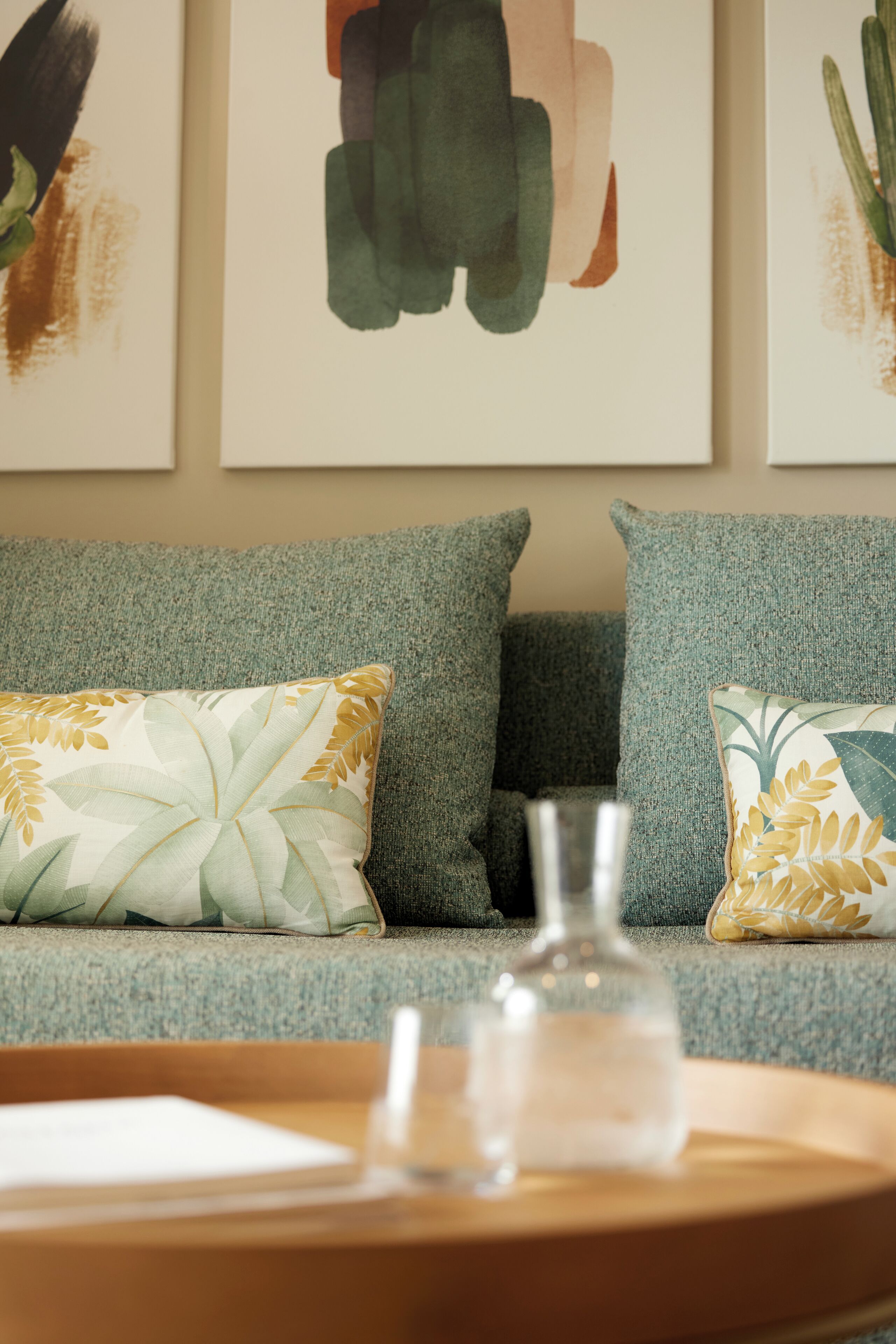 A living room with a grey sofa, two patterned cushions, a clear glass bottle, and a wooden tray.