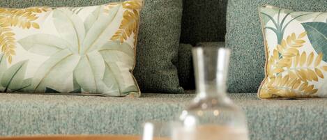 A living room with a grey sofa, two patterned cushions, a clear glass bottle, and a wooden tray.