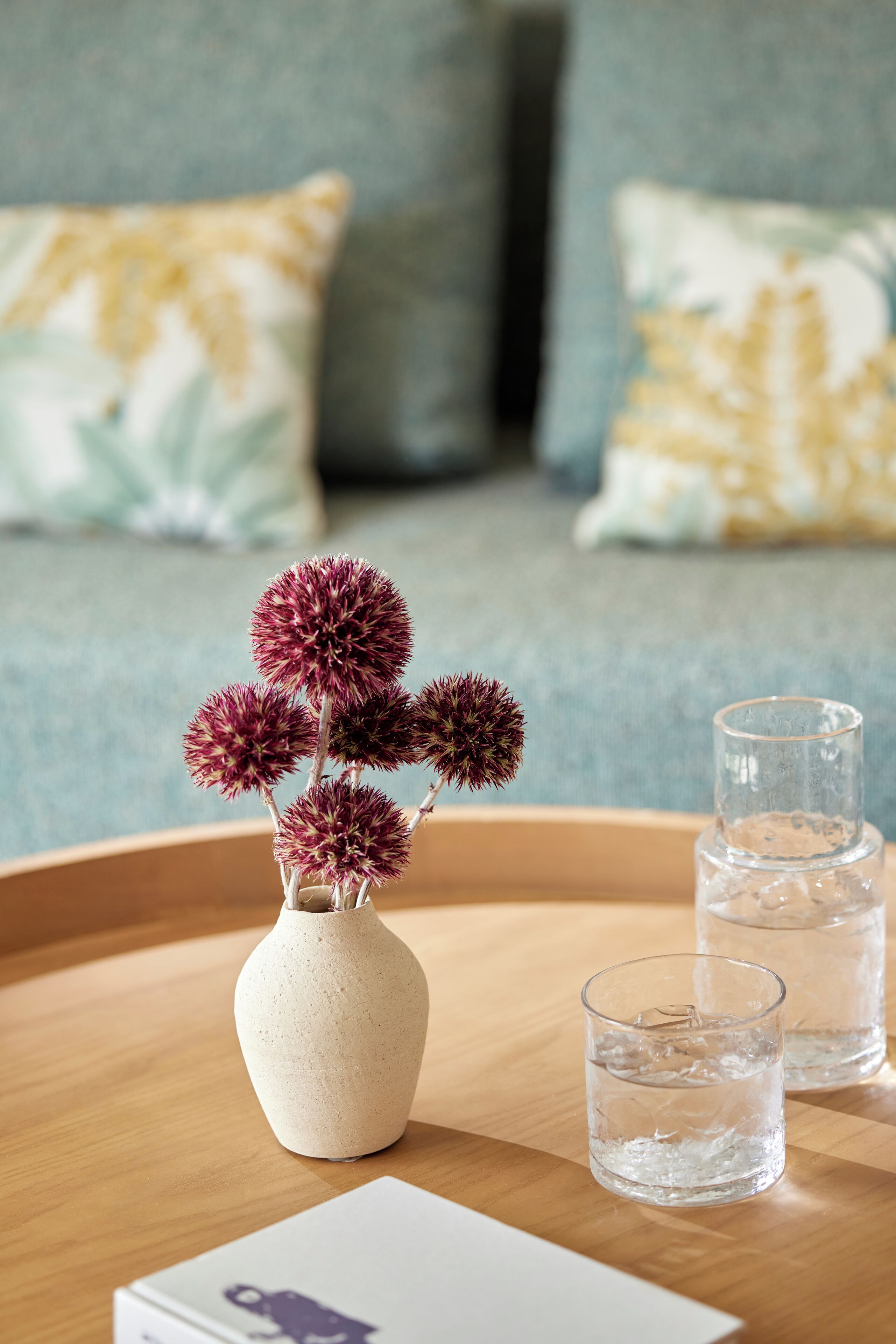 A wooden tray with a vase of purple flowers, two glasses of water, and a card on a wooden surface.