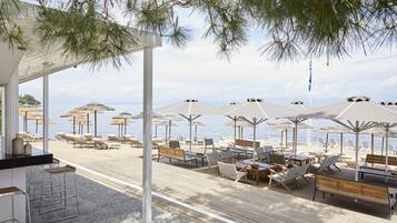 A beachside lounge with wooden deck seating, umbrellas, and a view of the sea.