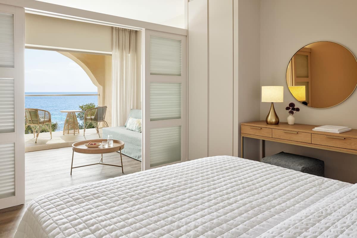 Ein Hotelzimmer mit Bett, Schreibtisch, Stuhl, einem kleinen Tisch und Meerblick.