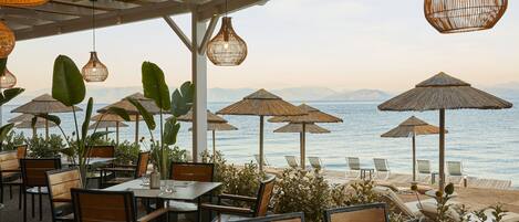 An outdoor seating area with tables and chairs, umbrellas, and a view of the sea.