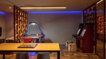 Una habitación con una mesa de ajedrez, una mesa de billar y una zona de videojuegos.