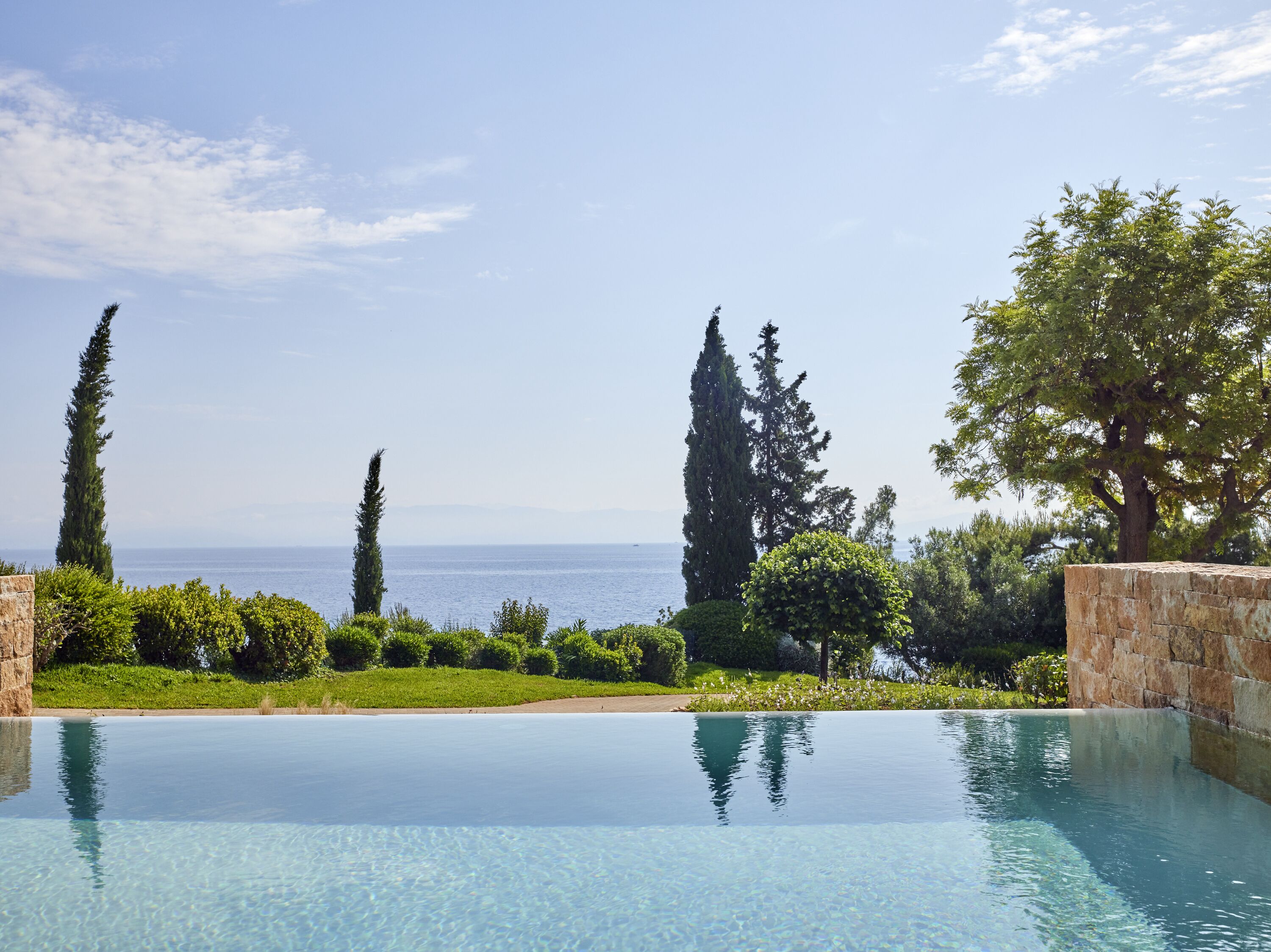 Una vista despejada de una piscina infinita con el mar y árboles altos al fondo.