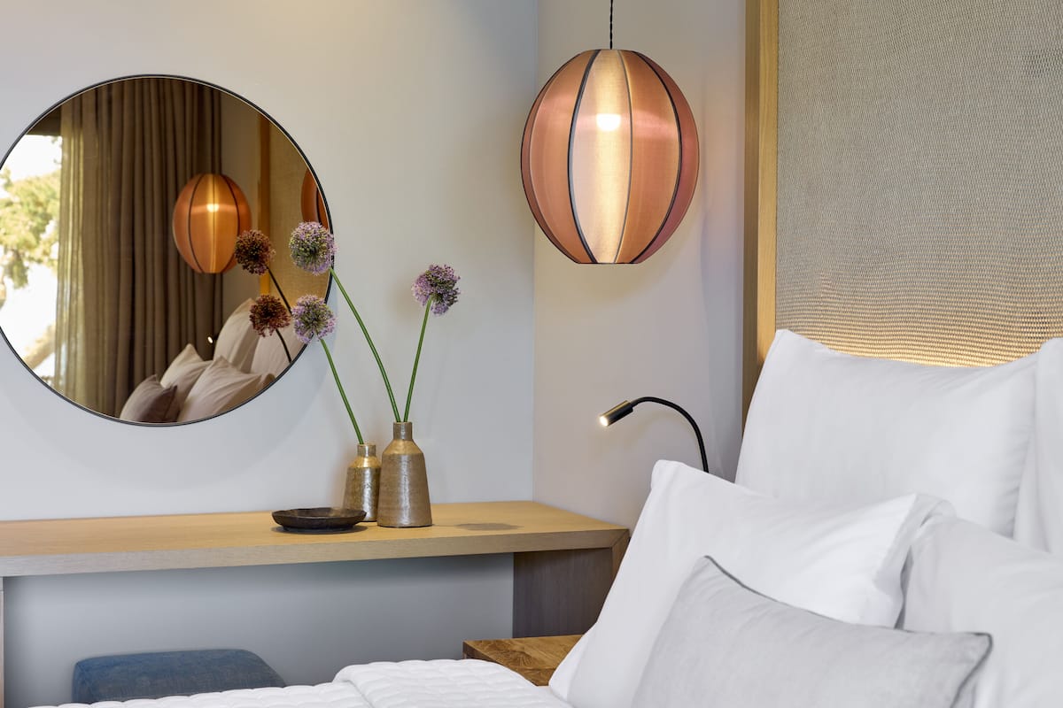 Ein modernes Schlafzimmer mit Bett, Nachttisch, Spiegel und einer hängenden Pendelleuchte.
