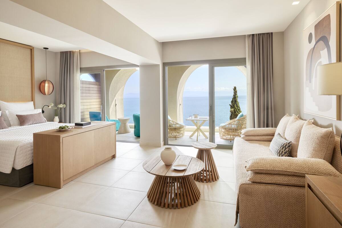 Ein modernes Hotelzimmer mit Bett, Schreibtisch, Sofa und einem Balkon mit Meerblick.