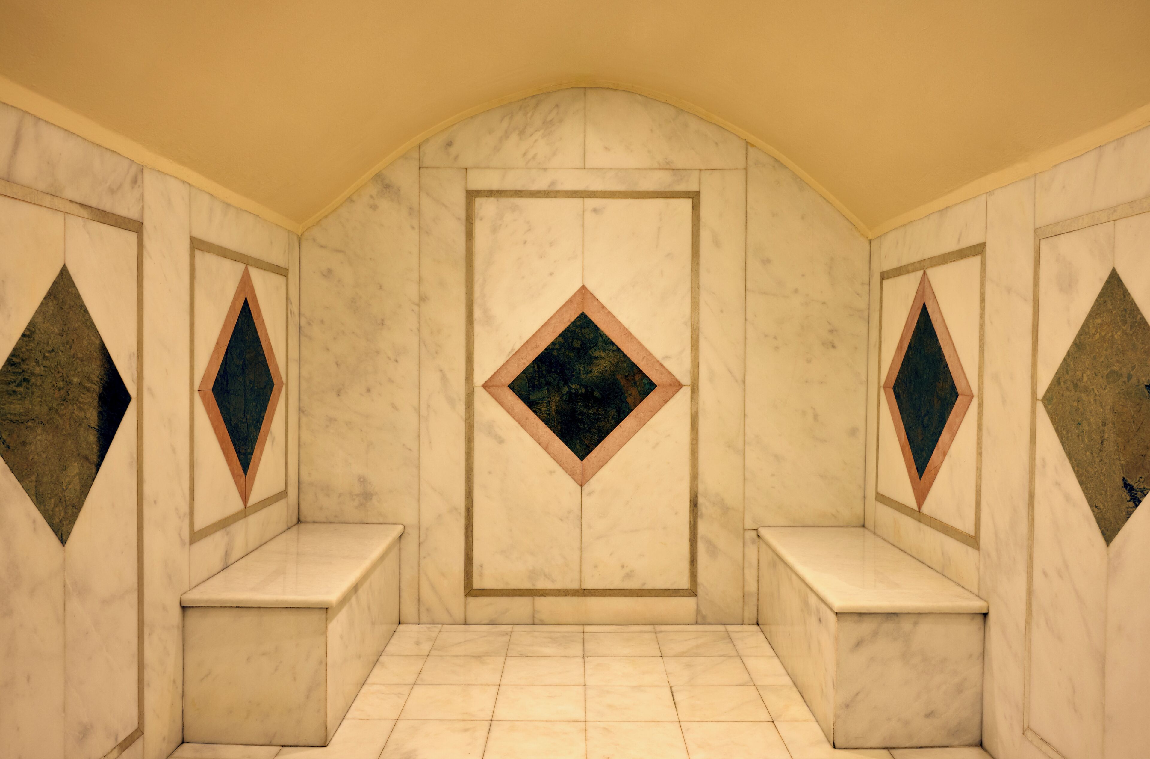 Una habitación con pared de mármol, una puerta central y dos bancos.