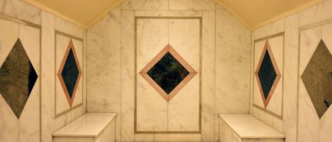 Una habitación con pared de mármol, una puerta central y dos bancos.