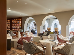 A spacious lounge area with multiple seating options, a well-stocked library, and large arched windows providing natural light.