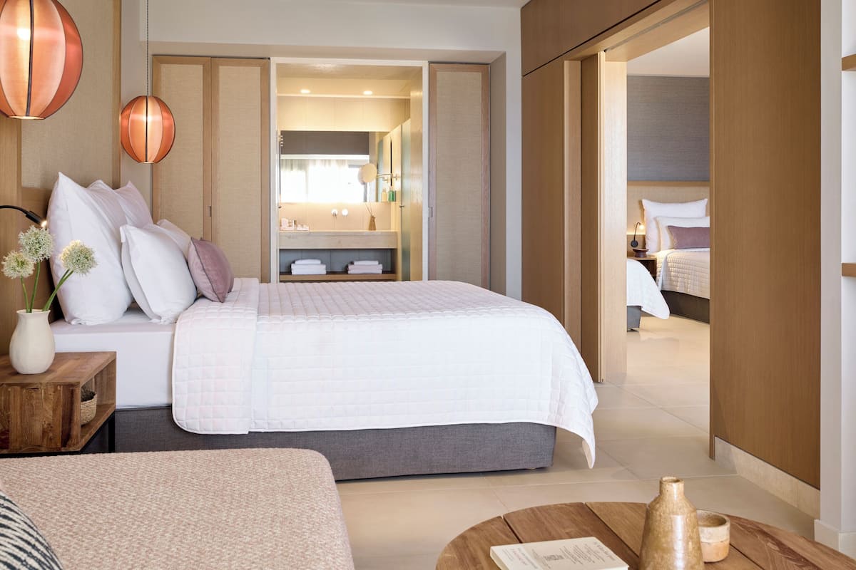 Ein modernes Hotelzimmer mit einem großen Bett, einem Nachttisch mit einer Vase und Blick ins Badezimmer.