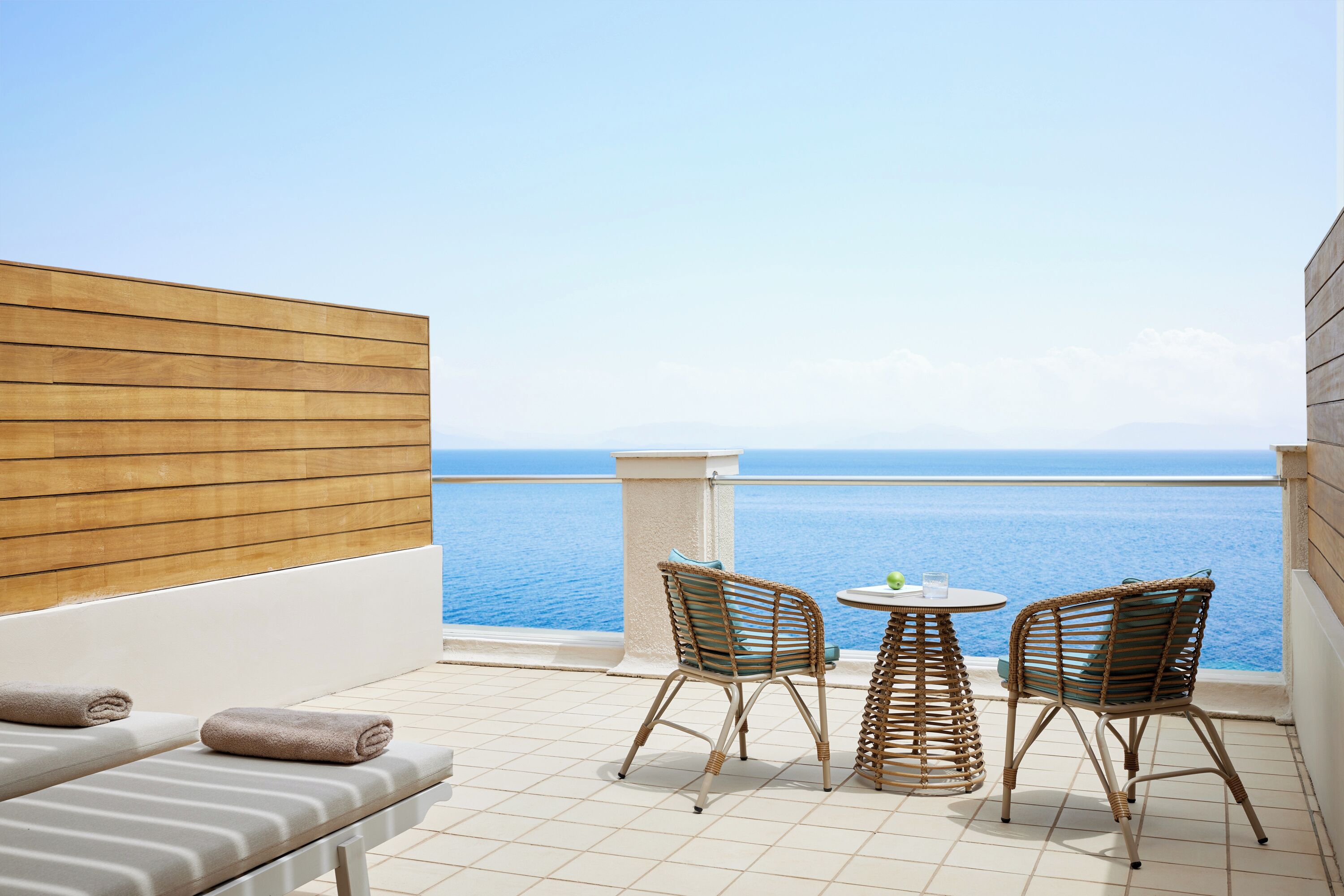 A balcony with two wicker chairs, a small round table, and a sofa with towels.