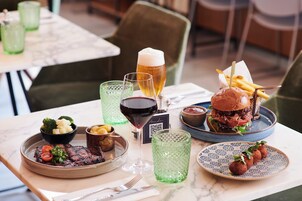 Ein Esstisch mit verschiedenen Speisen, darunter ein Steak, Pommes und ein Burger, sowie mehreren Gläsern Getränke.