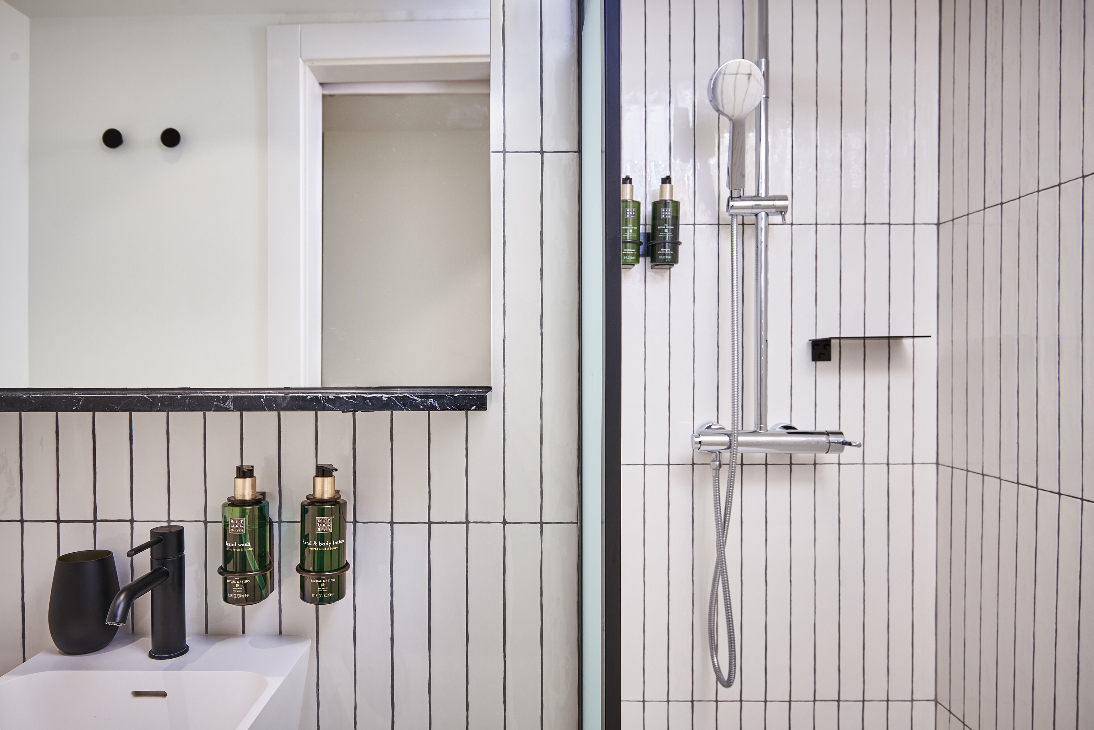 Un baño con un lavamanos blanco, grifo negro y dos botellas verdes en la pared.