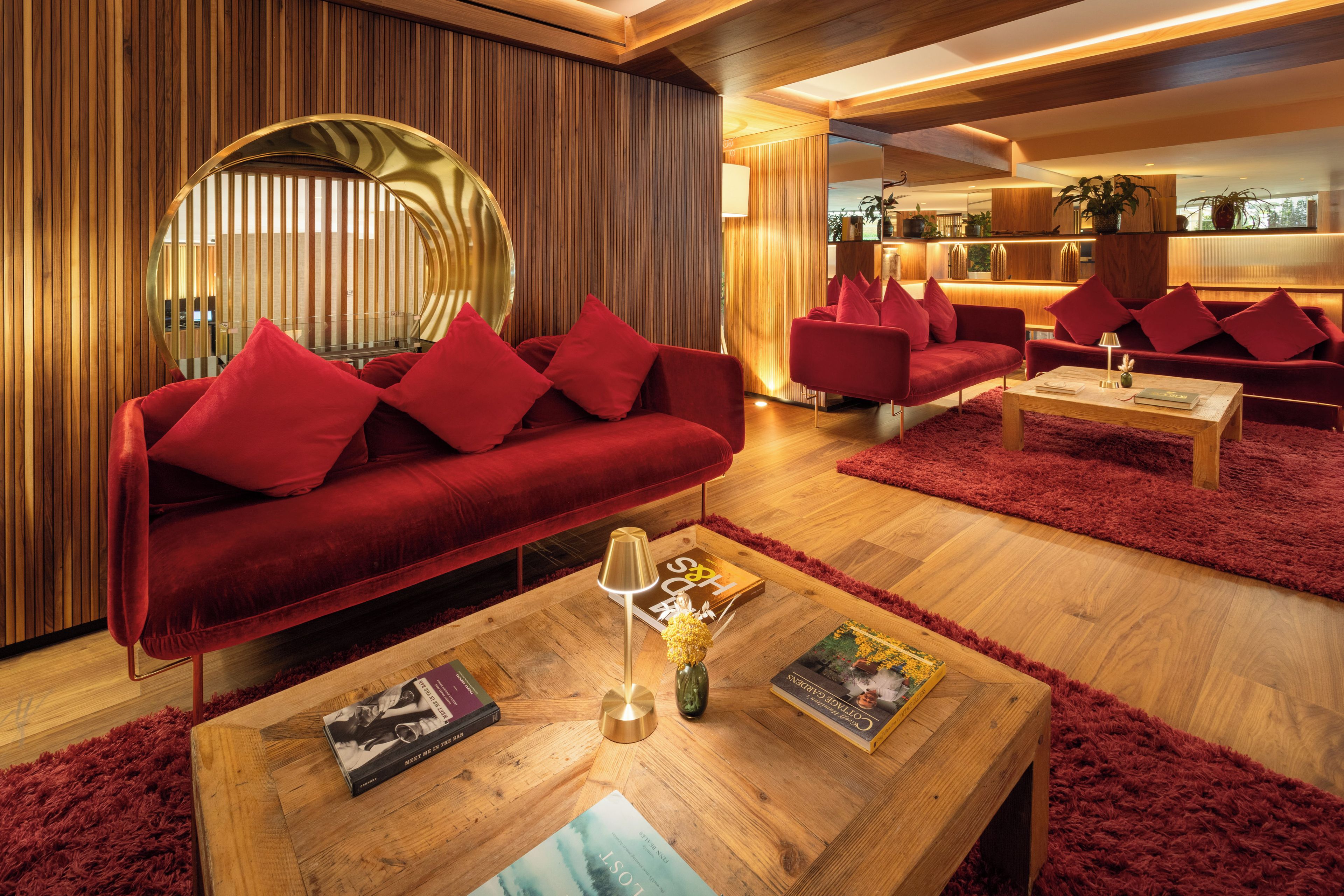 A modern living room with a red sofa, matching cushions, and a round mirror.