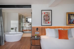Ein modernes Hotelzimmer mit einer großen Badewanne, einem ordentlich bezogenen Bett und einem kleinen Tisch mit einer Pflanze.