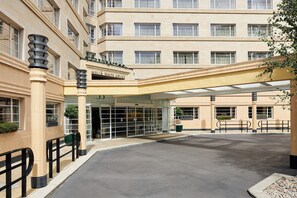 Ein Hotel mit Eingangsbereich, überdachtem Gang, Glastüren und einer beigefarbenen Fassade.