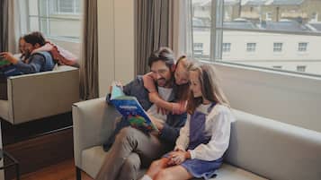 Et moderne hotelværelse med et stort vindue, en sofa og et spejl der reflekterer rummet.