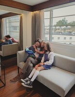 Ein modernes Hotelzimmer mit großem Fenster, einer Couch und einem Spiegel, der den Raum widerzuspiegeln scheint.