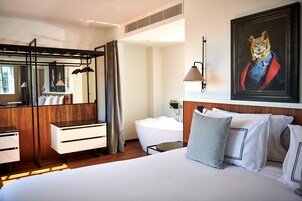A hotel room with a bed, a desk, a chair, a bathtub, and a large mirror.