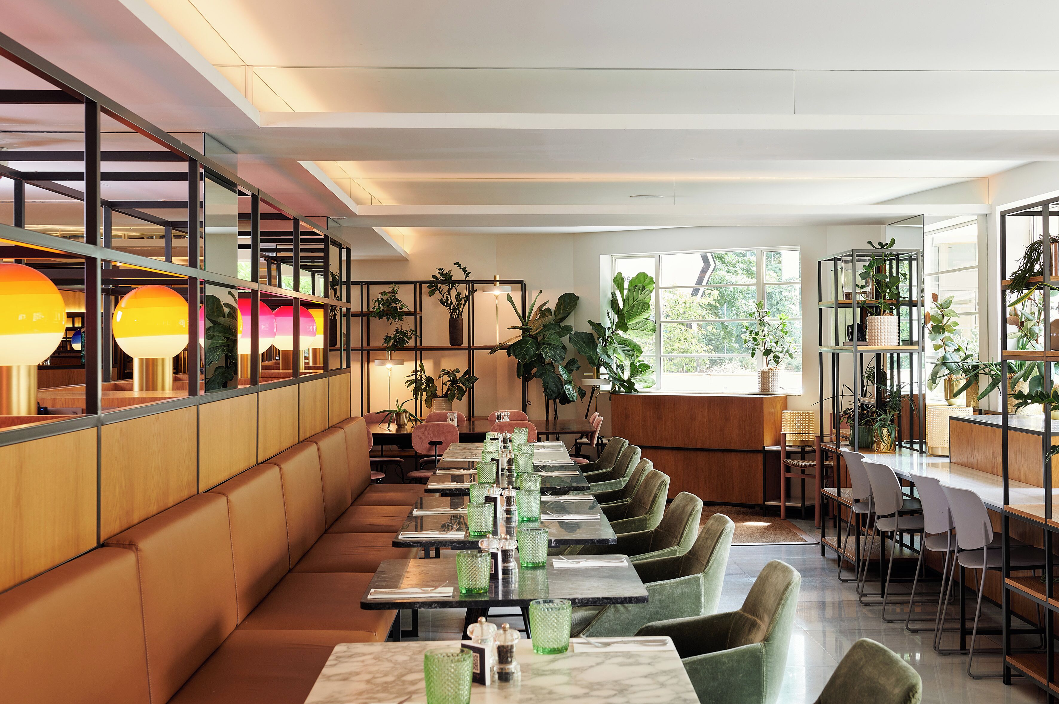 A modern restaurant with long tables, cushioned seating, and potted plants.