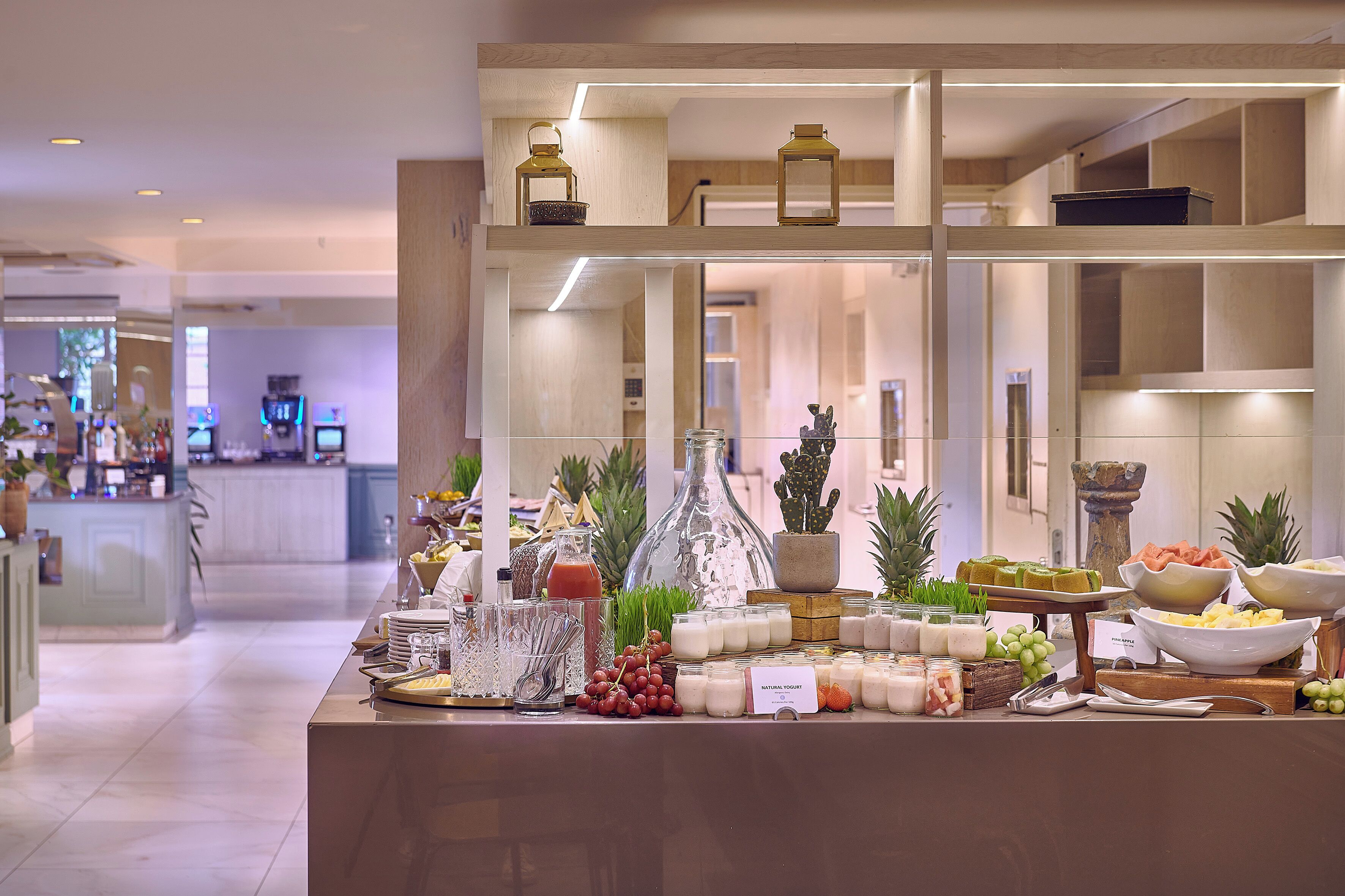 A buffet setup with various food items and beverages, including fruits, cheeses, and condiments, arranged on a counter with a modern design.