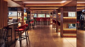 Zona de bar moderna con suelo de madera, taburetes rojos y una barra.