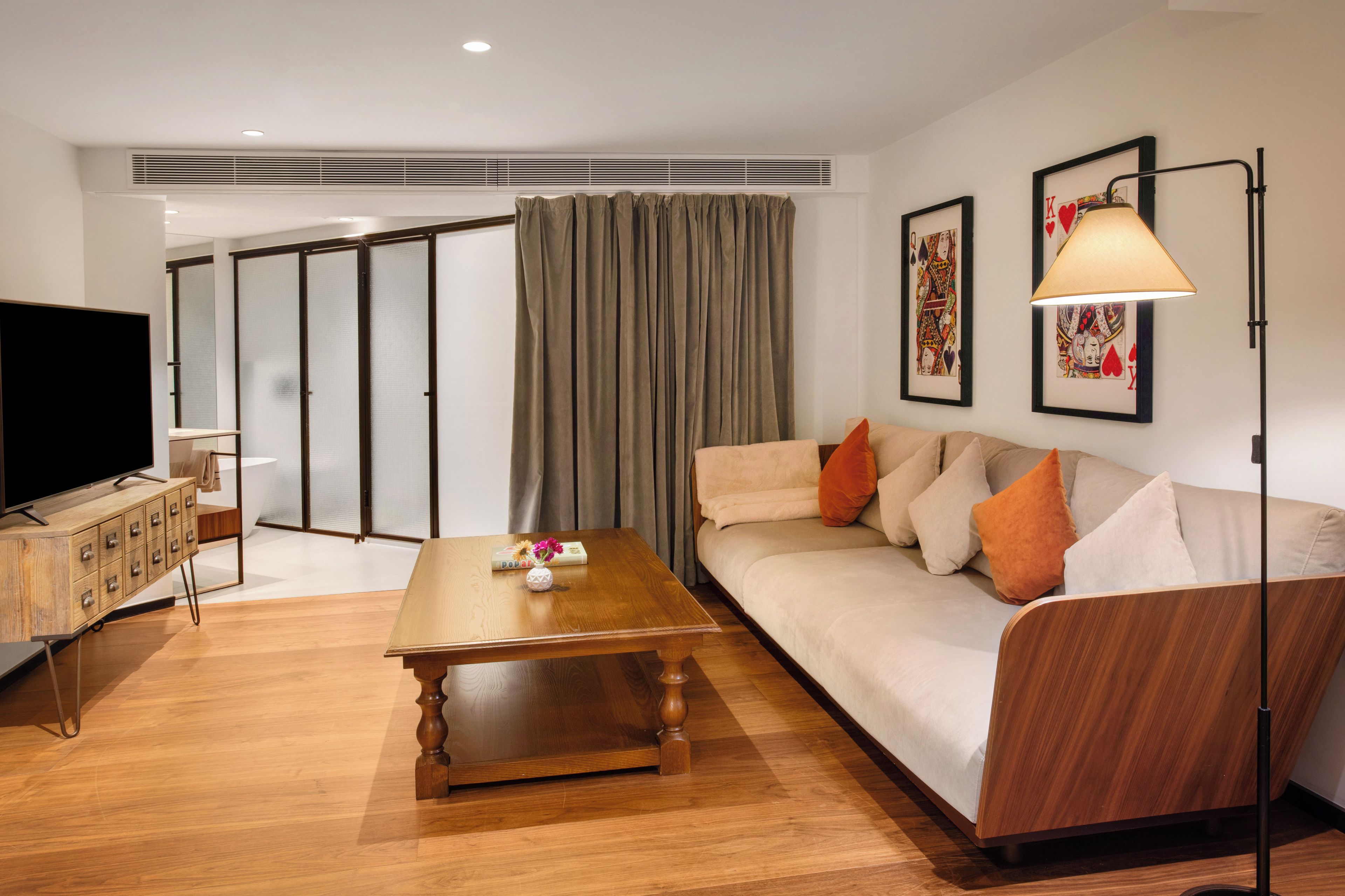 A modern living room with a wooden coffee table, a sofa with cushions, a television on a wooden cabinet, and artwork on the walls.
