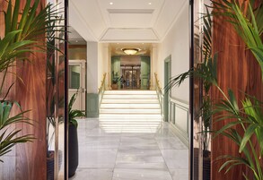 A hotel lobby with a marble floor, wooden paneling, and potted plants.