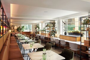 Ein modernes Restaurant mit langen Gemeinschaftstischen, einzelnen Sitzecken und verschiedenen Pflanzen.
