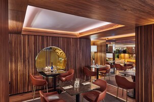 Een modern restaurantinterieur met houten lambrisering, ronde tafels en lederen stoelen.