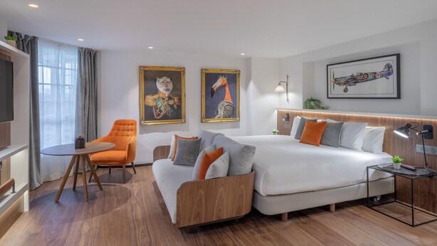 Una habitación de hotel moderna con sofá, sillón, cama y obras de arte en las paredes.