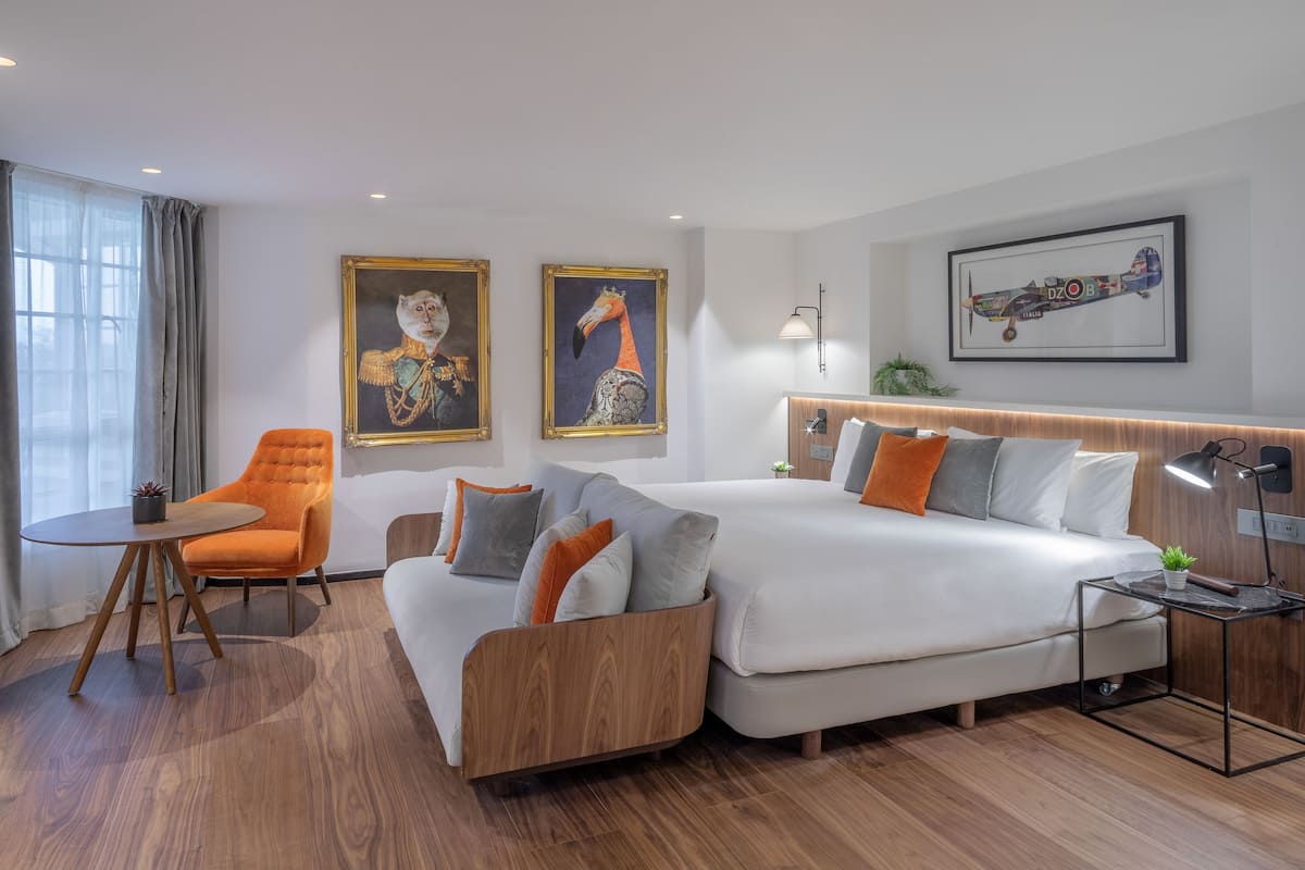 A modern hotel room with a sofa, a chair, a bed, and artwork on the walls.