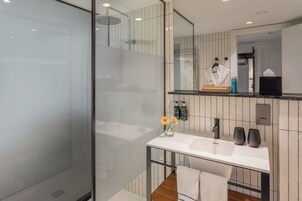 Ein modernes Badezimmer mit Duschkabine aus Glas, einem weißen Waschbecken mit Spiegel darüber und Toilettenartikeln auf der Ablagefläche.
