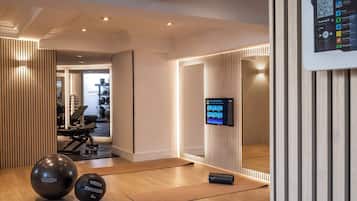 Un gimnasio moderno con equipo de ejercicio, una pantalla digital y suelo de madera.