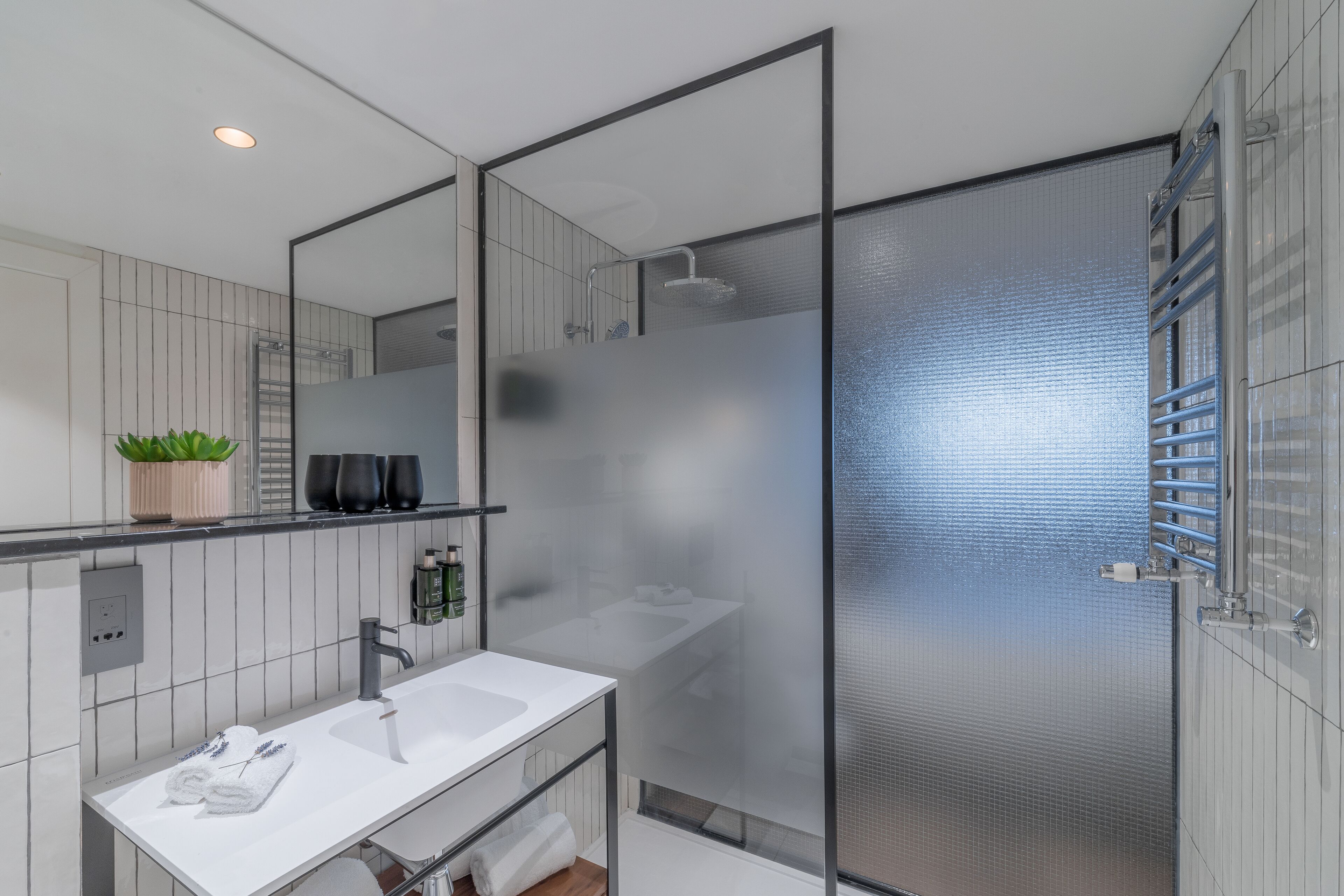 Un baño moderno con lavamanos blanco, espejo y cabina de ducha de vidrio.