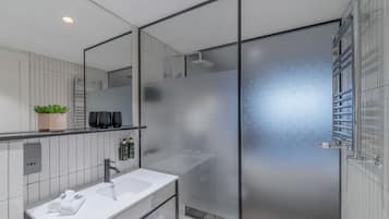 Un baño moderno con lavamanos blanco, espejo y cabina de ducha de vidrio.
