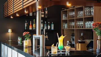 Angolo bar con un bancone nero, diverse bottiglie, bicchieri e un vaso con fiori.