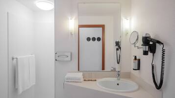 Un baño moderno con un lavabo blanco, un espejo, un secador de pelo y un perchero para toallas.