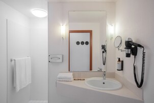 Un baño moderno con un lavabo blanco, un espejo, un secador de pelo y un perchero para toallas.