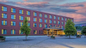 Ett hotell byggt av rött tegel med en modern fasad, en överbyggd entré och en rymlig innergård med träd.