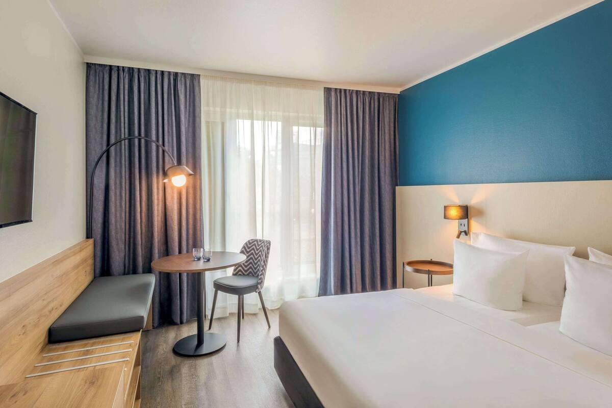 A hotel room with a bed, a desk, a chair, and a sofa.