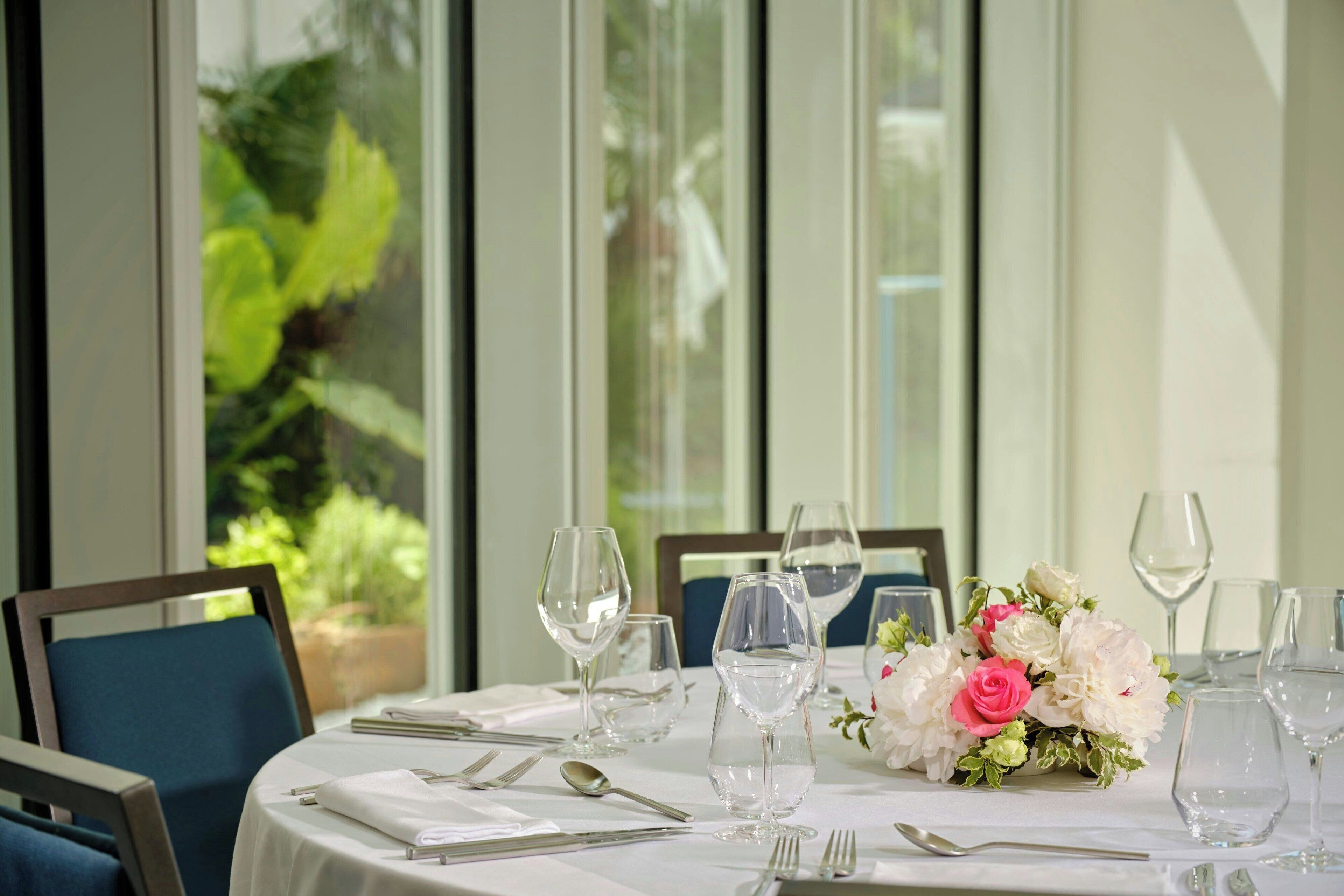 A dining table set for six with white tablecloth, clear glassware, and a floral centerpiece.