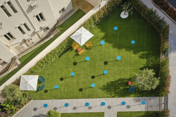 An aerial view of a courtyard with a lawn, seating areas, and a building in the background.