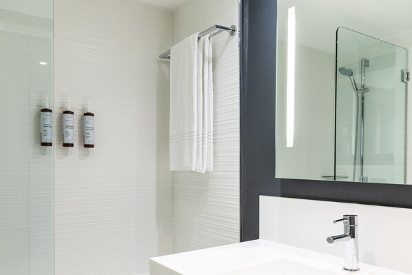 A modern bathroom with a glass shower enclosure, a white sink, and a large mirror.