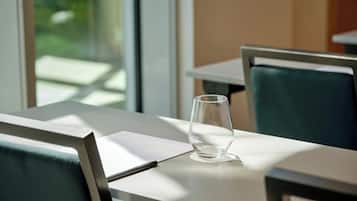 A table with a glass of water, a pen, and a notepad in a bright room with a window.