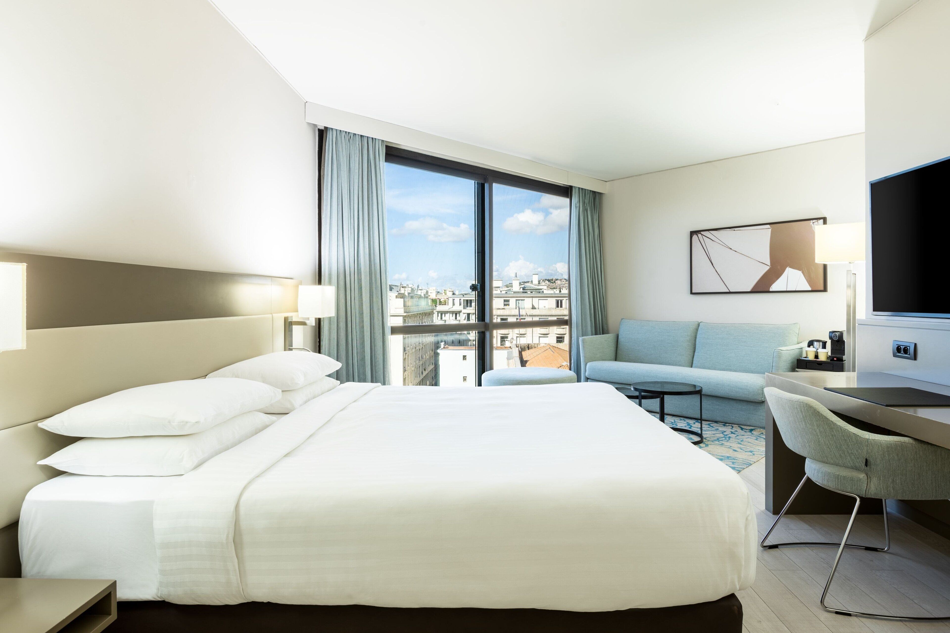 A hotel room with a large bed, a desk, a chair, a sofa, and a TV.