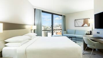 A hotel room with a large bed, a desk, a chair, a sofa, and a TV.