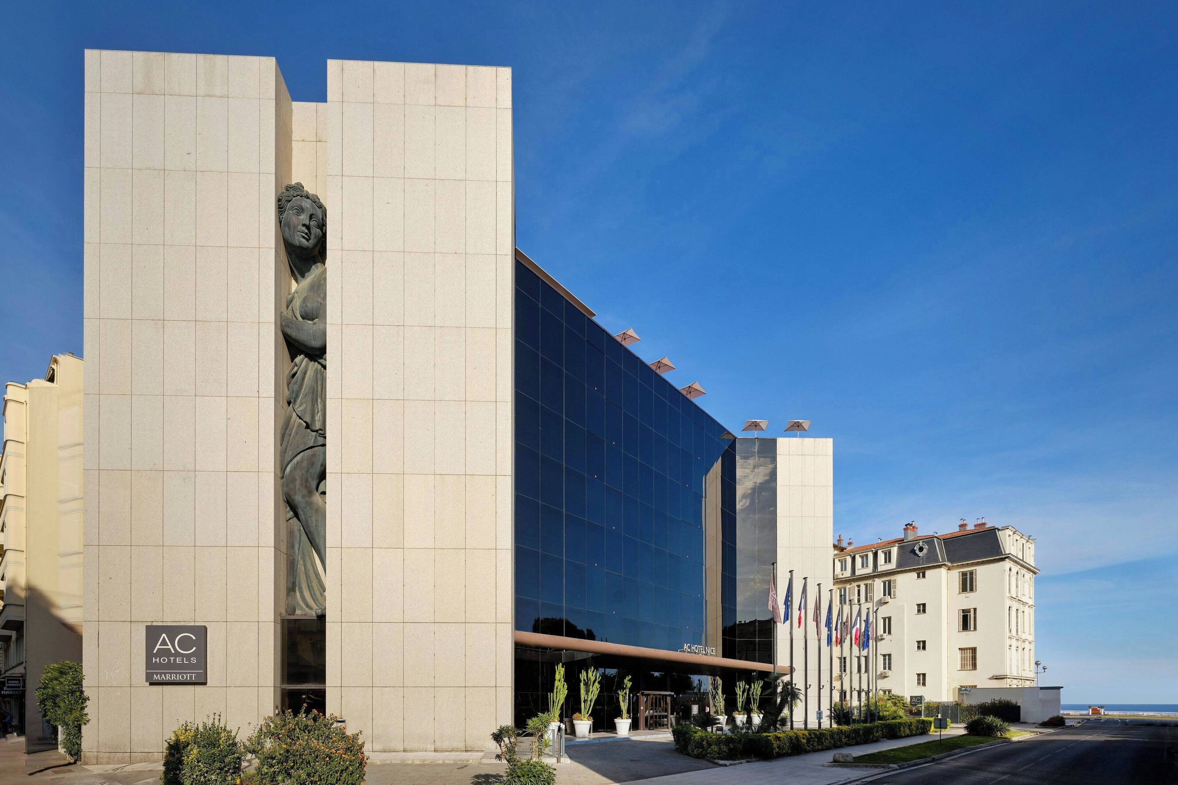 Un hotel moderno con una gran estatua en la fachada, una entrada de vidrio y banderas afuera.