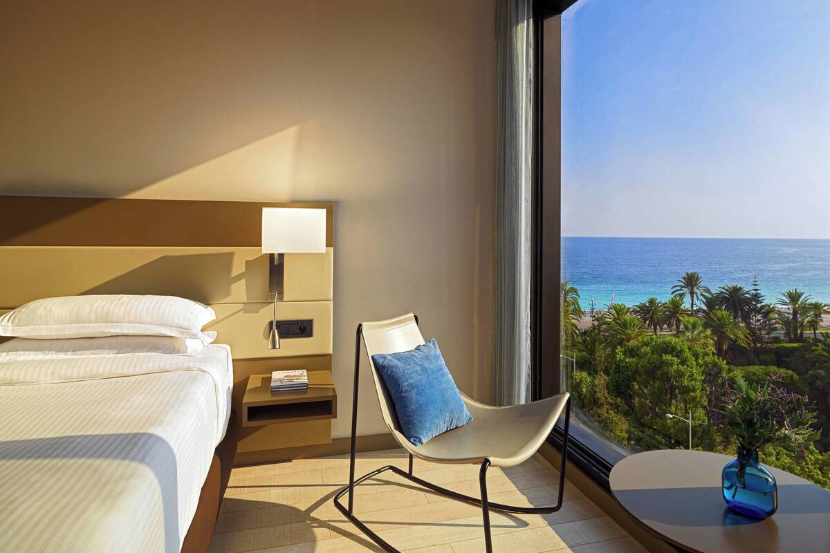 A hotel room with a bed, a chair, a small table, and a view of the ocean.
