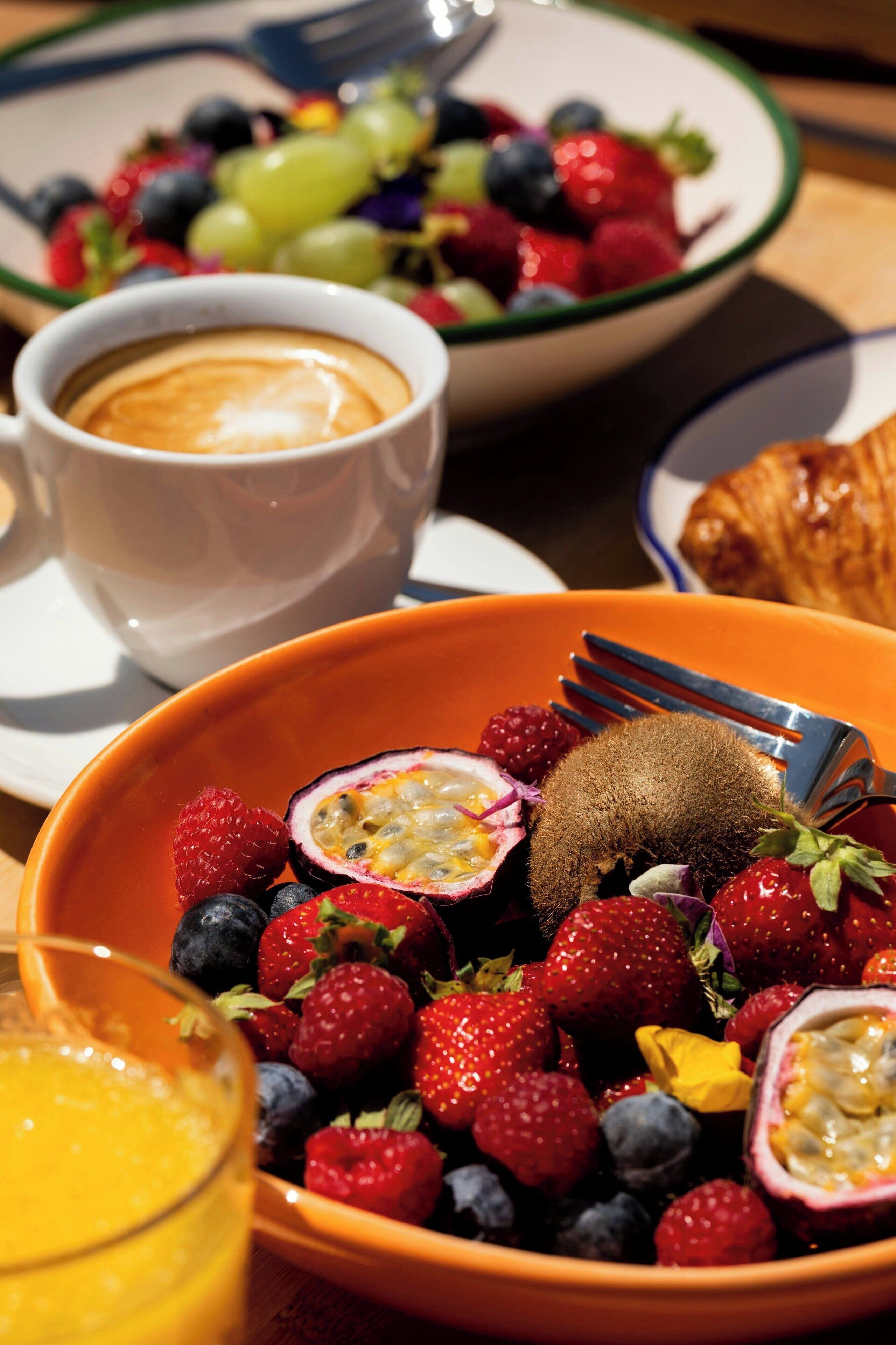 Colazione con una ciotola di frutti di bosco misti e frutto della passione, una tazza di caffè e un croissant su un tavolo.